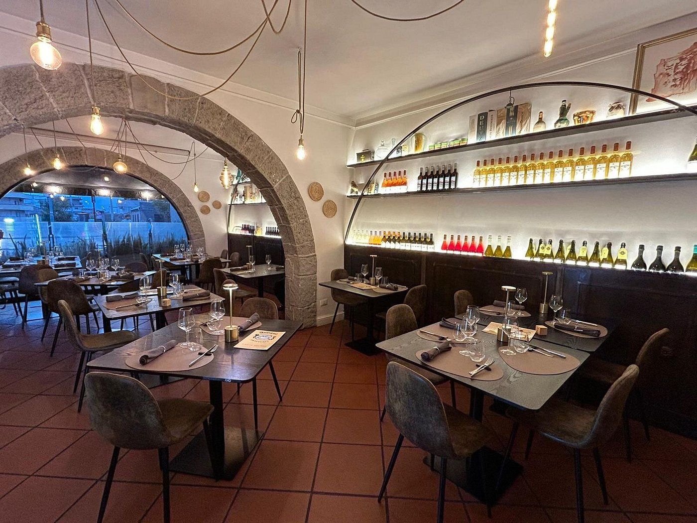 La sala interna con archi in pietra, pavimento in cotto e la parete dei vini illuminata